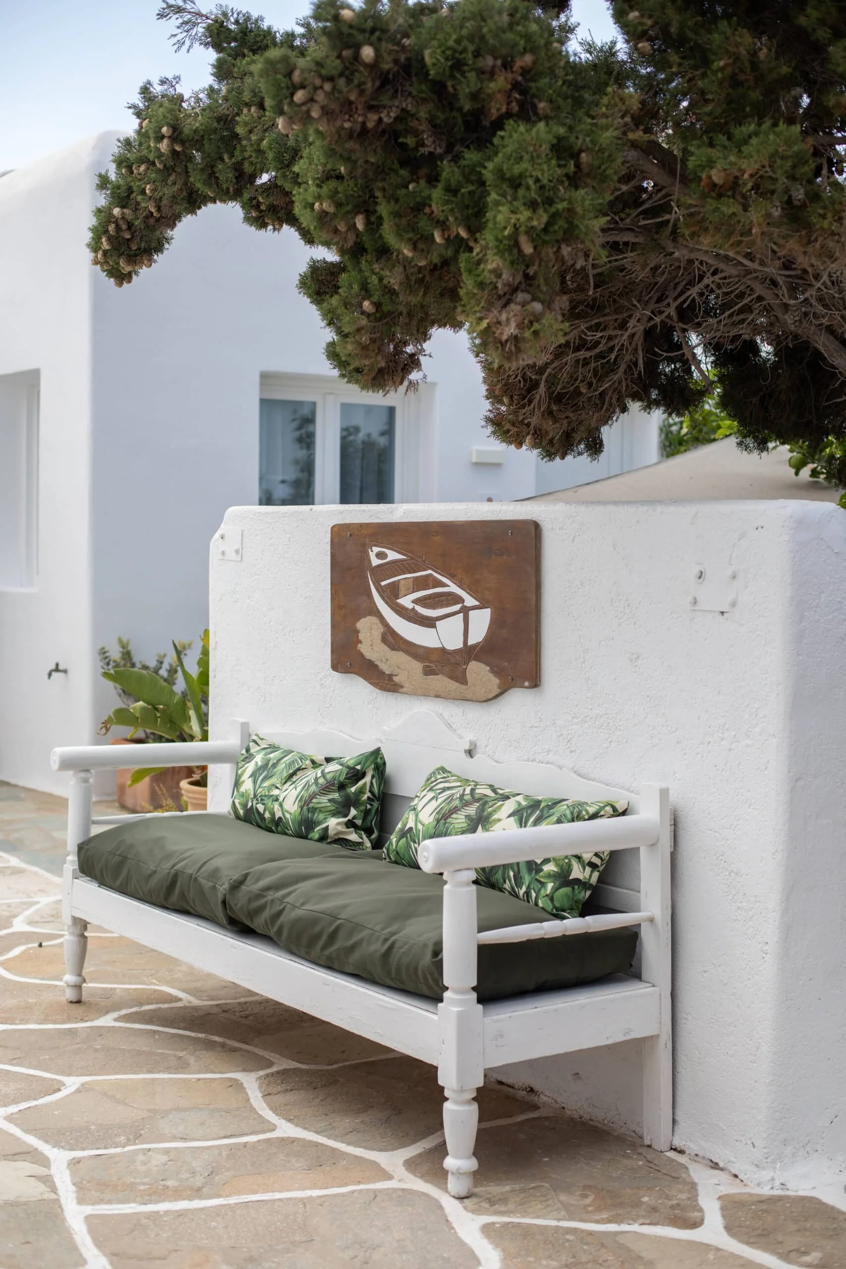 White garden bench with green cushions beneath a boat mosaic